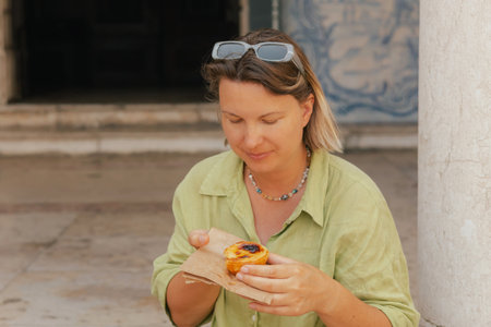 Gen Z middle age woman tries Portuguese egg tart pastry called Pastel de Nata near bakery in Lisbon....