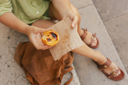 Gen Z middle age woman tries Portuguese egg tart pastry called Pastel de Nata near bakery in Lisbon....