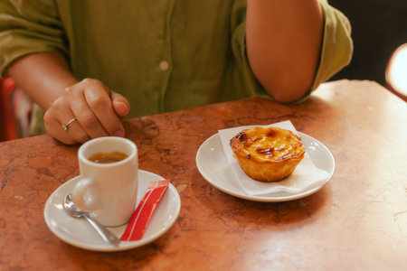 Close up middle age woman tries Portuguese egg tart pastry called Pastel de Nata with coffee near...