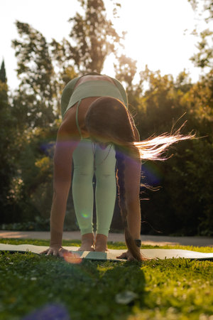 Young woman in sportswear stretching body on fitness mat at public park, doing yoga. Healthy...