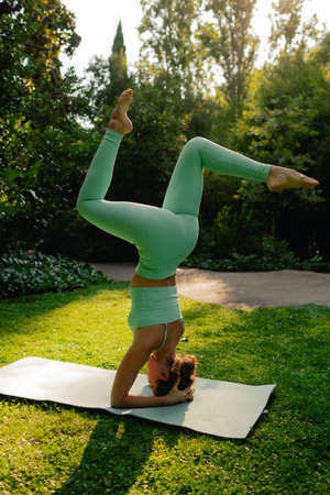 Young woman in sportswear stretching body on fitness mat at public park, doing yoga. Healthy...