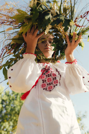 Close-up of Ukrainian girl in traditional blouse Vyshyvanka weaving a flower wreath for Ivana Kupala...