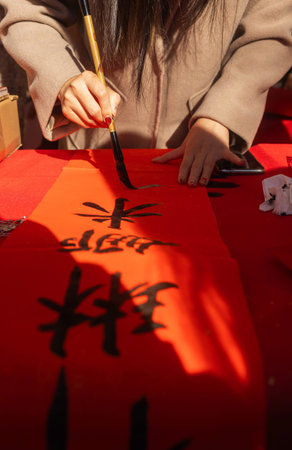 Close up of woman writing Happy New Year with Chinese calligraphy on couplets for celebration....