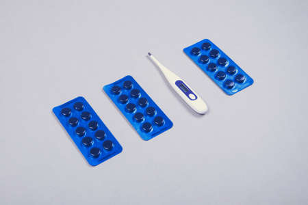 Pills blister and electronic thermometer on gray table, place for text, copyspace