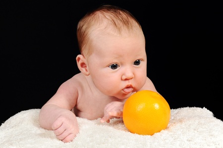 Newborn baby girl with orange lies on a white blanket, black backgroundの写真素材