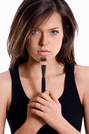 Portrait of a brunette woman applying makeup with brush on her face looking at cameraの写真素材