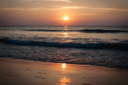Colorful sunset on the sea shore and footprints in the sandの写真素材
