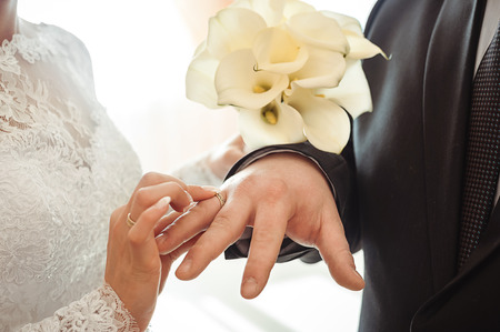 bride putting a wedding ring on the finger of the groomの写真素材