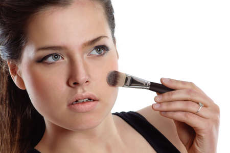 Portrait of a brunette woman applying makeup with brush on her faceの写真素材