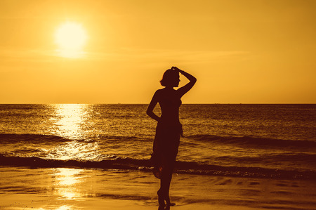 young woman stands on the beach during a beautiful sunsetの写真素材