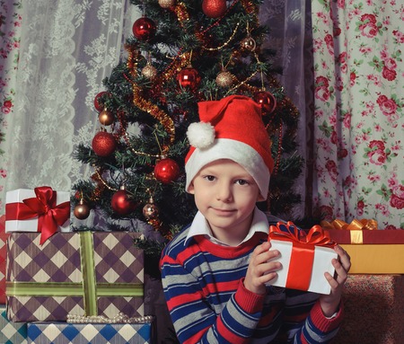 Photo of boy in Santa cap holding gift box with red bow in his hands. Christmas concept.の写真素材