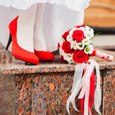 female feet in red wedding shoes with a bouquet of red rosesの写真素材