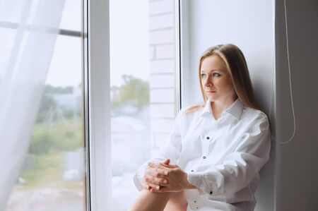 Portrait of a woman in a white shirt looking out the windowの写真素材