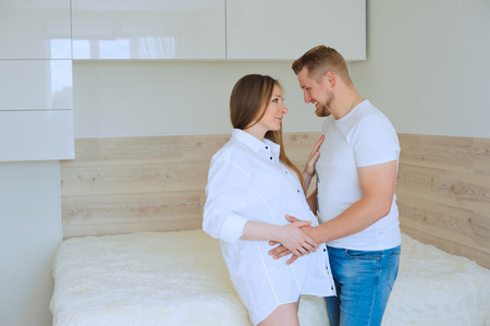 happy pregnant woman and her husband together caressing her pregnant belly at homeの写真素材