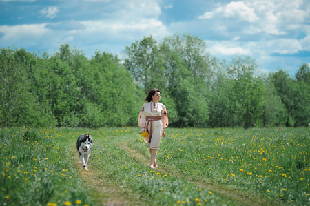 Portrait of a beautiful girl in Slavic clothes. Young woman with a Siberian husky dog. Summertimeの写真素材