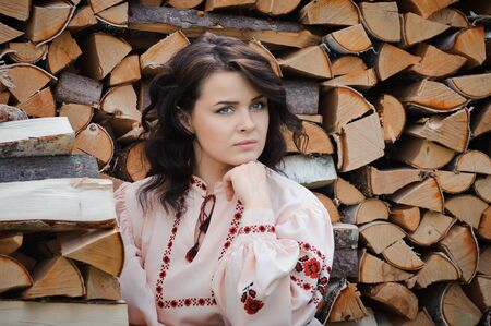 Portrait of a beautiful girl in Slavic clothes on the background of a woodpile. Summertimeの写真素材