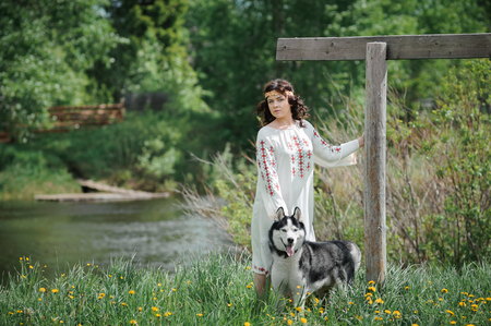 Portrait of a beautiful girl in Slavic clothes. Young woman with a Siberian husky dog. Summertimeの写真素材
