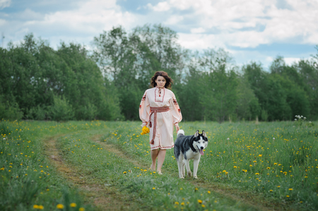 Portrait of a beautiful girl in Slavic clothes. Young woman with a Siberian husky dog. Summertimeの写真素材