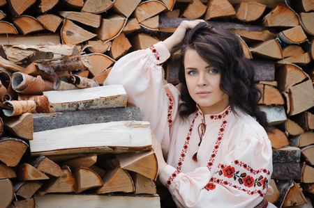 Portrait of a beautiful girl in Slavic clothes on the background of a woodpile. Summertimeの写真素材