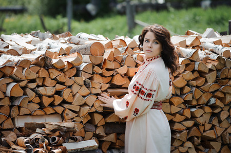 Portrait of a beautiful girl in Slavic clothes on the background of a woodpile. Summertimeの写真素材