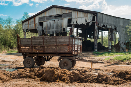 Old wooden wagon in front of an abandoned countryside barn. Destruction and decline of small peasant farmsの写真素材
