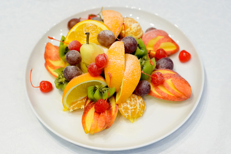 Sweet fresh fruits on white plate. Orange, apple, grapes, pear, kiwi, cherry Healthy food styleの写真素材