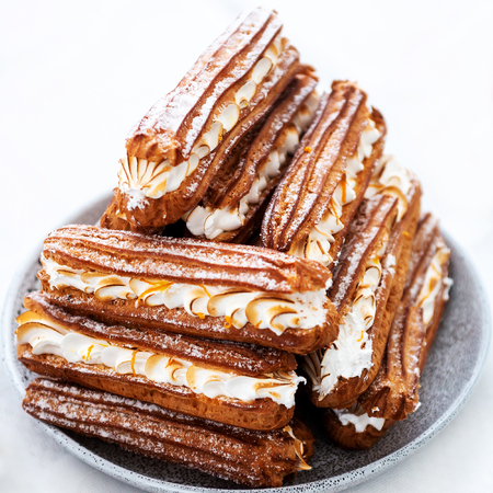Tasty fresh cream cakes on a plate. Eclairs with custard. Traditional French dessert. Selective...