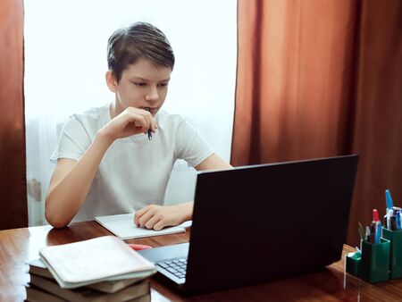 Student looking at computer, watching online education classes or webinar at home. Schoolboy...