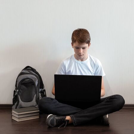 Student sitting on the floor with legs crossed and using laptop. Distance and e-learning education concept, online lessons. Social distance during quarantineの写真素材