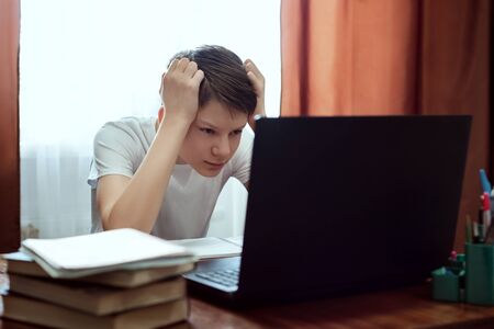 Tired student looking at computer, watching online education classes at home. Schoolboy studying...