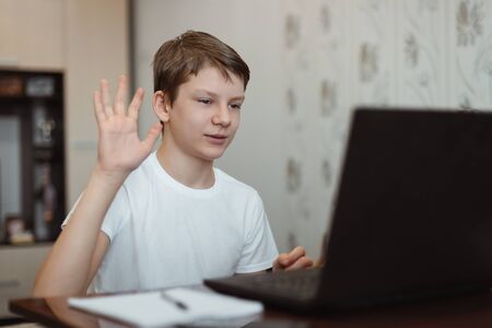 Happy boy using laptop computer to communicate with friends on the Internet at home and waving hand. Online video chat. Social distance during quarantineの写真素材