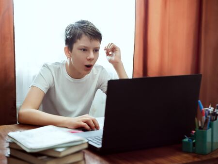 Surprised student looking at computer, watching online education classes at home. Schoolboy studying with laptop and doing school homework. Distance and e-learning education concept, online lessonsの写真素材