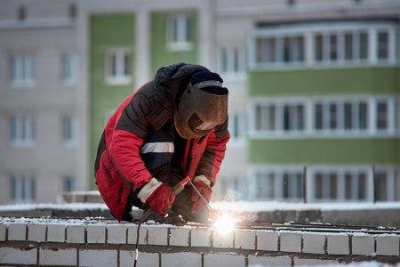 Welder wearing a protective mask. Industrial worker in red uniform at a construction site. Welding workの写真素材