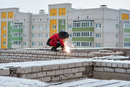 Welder wearing a protective mask. Industrial worker in red uniform at a construction site. Welding workの写真素材