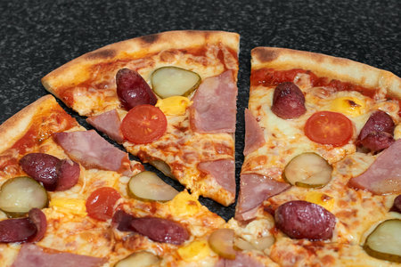 Sliced pizza with sausage, ham, pickles and tomatoesの写真素材