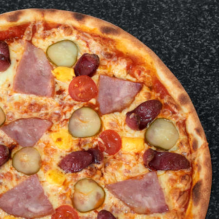 Tasty pizza with sausage, ham, pickles and tomatoesの写真素材