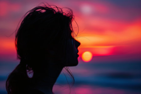 A woman with long hair is looking out at the ocean. The sky is a beautiful mix of pink and orange hues, creating a serene and peaceful atmosphereの素材