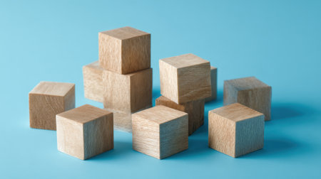A collection of wooden cubes is arranged on a light blue surface. The blocks vary in height and create an interesting pattern, showing their natural texture.の素材