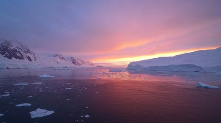 A stunning sunset casts vibrant colors across the icy waters of Antarctica. The sky transitions from orange to purple, illuminating the landscape. Icebergs float peacefully in the foreground.の素材