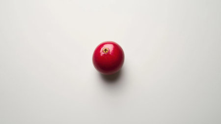 A red fruit is shown on a white background. The fruit is round and has a stem. Concept of freshness and natural beautyの素材