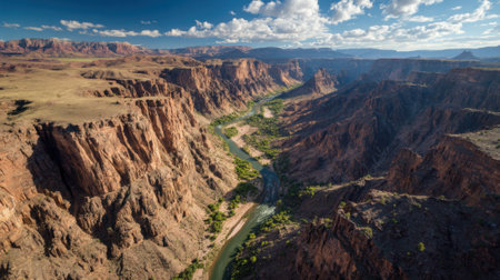 A breathtaking view of a canyon featuring steep rock formations and a winding river flowing below. Sunlight illuminates the landscape highlighting its stunning colors and shapes.の素材