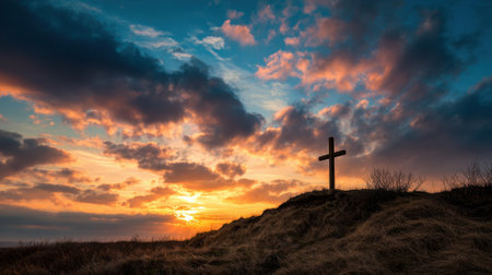 A cross is standing on a hillside in front of a beautiful sunset. The scene is serene and peaceful, with the sun setting in the background and the cross standing tall and proudの素材