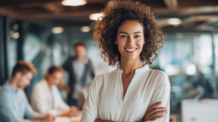 A woman with curly hair is smiling and posing for a picture in a business setting. She is wearing a white shirt and has her arms crossed. The scene suggests a professional and confident atmosphereの素材