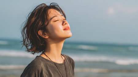 A young woman stands on the beach eyes closed savoring the peaceful ocean air at sunset.の素材