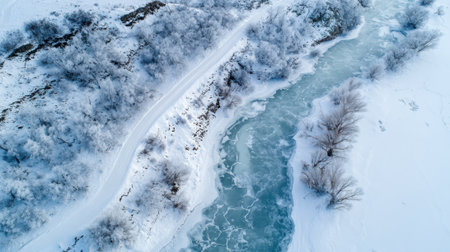 A snow-covered river winds through frost-laden trees under a clear sky. The tranquil scene captures the beauty of winter, showcasing nature's serene charm in a peaceful landscape.の素材