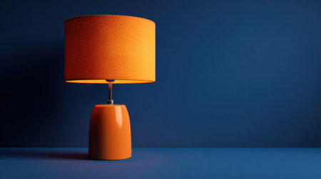 A bright orange lamp stands on a blue surface, showing its unique design and warm light. The simple yet striking color combination enhances the decor of the space.の素材