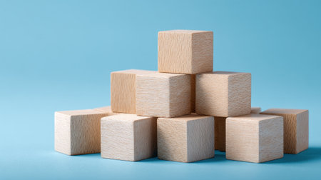 A collection of wooden blocks is stacked to form a pyramid-like structure. The light blue background adds a playful and inviting atmosphere, perfect for imaginative play.の素材