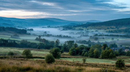 Soft mist rises over green valleys and hills at dawn creating a peaceful and dreamy atmosphere.の素材
