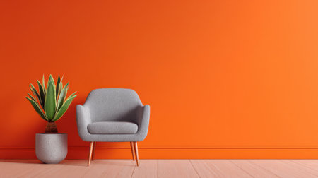 A gray chair sits beside a bright orange wall and a decorative plant in a clean inviting room.の素材
