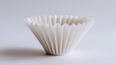 A white paper cupcake wrapper is sitting on a white background. The cupcake wrapper is folded in a way that it looks like a small bowlの素材